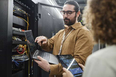 IT-Fachleute diskutieren über Daten auf Laptop und Tablet-PC im Serverraum - KPEF00488