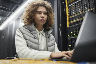 Ingenieur mit lockigem Haar arbeitet am Laptop im Serverraum - KPEF00494