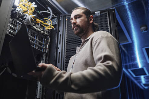 Ingenieur arbeitet an einem Laptop in der Nähe der Serverraumausrüstung - KPEF00502