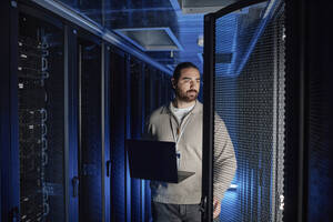Ingenieur, der einen Laptop hält und einen Supercomputer im Serverraum untersucht - KPEF00510