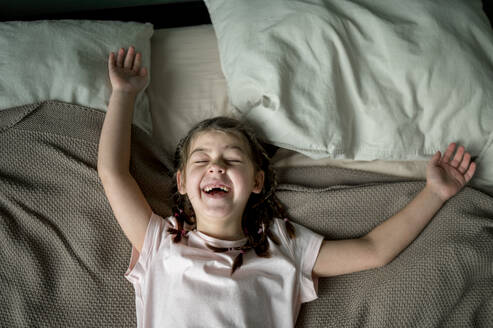 Mädchen auf dem Bett liegend und lachend zu Hause - ANAF02498