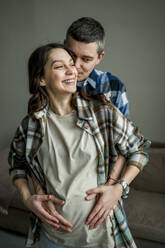 Liebender Mann hält Hände der schwangeren Frau auf dem Bauch zu Hause - ANAF02501
