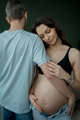 Mann und schwangere Frau umarmen sich vor grünem Hintergrund - ANAF02515