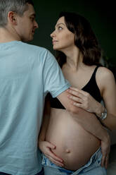 Liebender Mann und schwangere Frau schauen sich vor dunklem Hintergrund an - ANAF02516