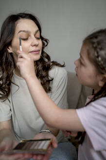 Girl applying eye make-up on mother at home - ANAF02519