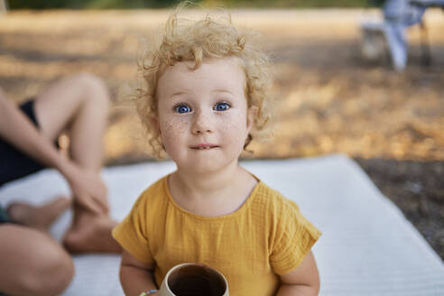 Nettes Mädchen mit Teetasse sitzt auf Picknickdecke im Park - ANNF00676