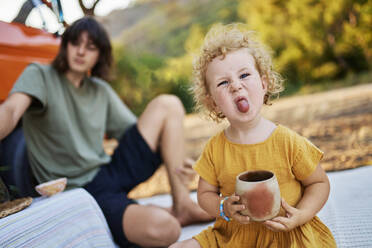 Nettes Mädchen mit Teetasse, die die Zunge herausstreckt, sitzt bei ihrem Bruder - ANNF00678