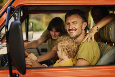 Glücklicher Mann mit Familie im Wohnmobil sitzend im Urlaub - ANNF00683