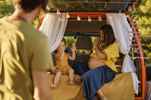 Vater betrachtet die schwangere Frau, die mit ihrer Tochter im Wohnmobil spielt - ANNF00788