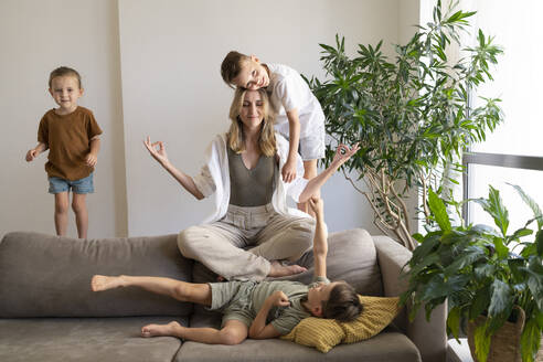 Mutter meditiert auf dem Sofa, während die Jungen zu Hause spielen - SVKF01780