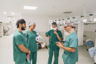 Chirurg mit Smartphone im Gespräch mit Kollegen im Krankenhaus - MMPF01017
