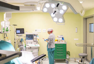 Nurse using smart phone near medical equipment in operating room - MMPF01020