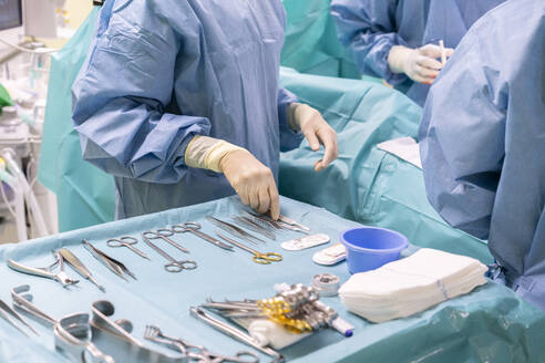 Nurse holding surgical tool with surgeons performing surgery on patient in emergency room - MMPF01030