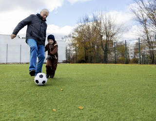 Enkel und Großvater haben Spaß beim Spielen mit dem Ball auf dem Fußballplatz - MBLF00169