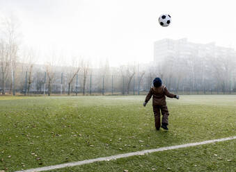 Junge wirft Ball in die Luft auf Fußballplatz - MBLF00171