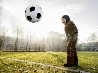 Glücklicher Junge spielt mit Ball auf Fußballplatz - MBLF00172