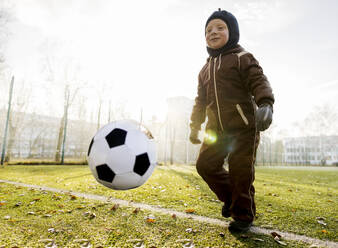 Lächelnder Junge spielt mit Ball auf einem Fußballplatz - MBLF00173