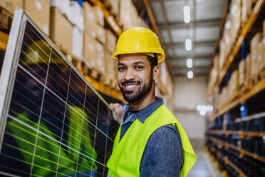 Happy warehouse worker carring a solar panel. - HPIF31219