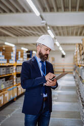 Manager in suit controlling goods in warehouse. - HPIF31229