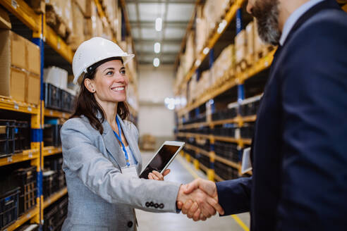 Managers in suits shaking hands in a warehouse. - HPIF31243