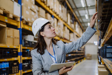 Manager woman in suit controlling goods in warehouse. - HPIF31246