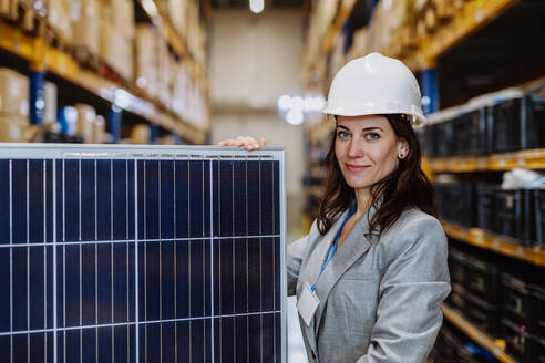 Porträt eines Managers mit einem Solarpanel in einem Lagerhaus. - HPIF31250