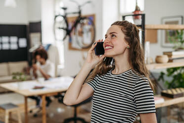 Young smiling woman calling in office, his colleague sitting in the background. - HPIF31306