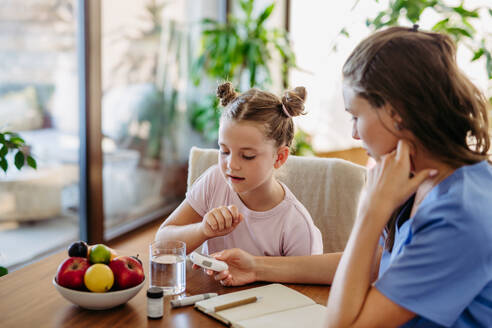 Mother checking girl's blood glucose level using a fingerstick glucose meter before meal. Diabetic girl waiting for results from blood test. - HPIF31351