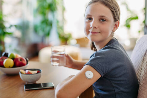 Nahaufnahme des Sensors eines kontinuierlichen Blutzuckermessgeräts am Arm eines Mädchens. Das Mädchen trinkt Wasser, um ihren Diabetes besser in den Griff zu bekommen. - HPIF31355