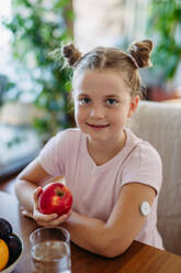 Porträt eines diabetischen Mädchens mit einem kontinuierlichen Glukosemessgerät, das auf seine Ernährung achtet. Der Apfel verursacht einen minimalen Anstieg des Blutzuckerspiegels. Das CGM-Gerät erleichtert das Leben des Schulmädchens und hilft ihr, ihre Krankheit zu bewältigen und sich auf andere Aktivitäten zu konzentrieren. - HPIF31358