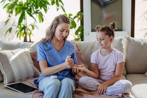 Nurse checking girl's blood glucose level using a fingerstick glucose meter. Endocrinologist waiting for results from blood test. - HPIF31364