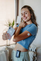 Beautiful diabetic girl taking a selfie, having an insulin pump and a continuous glucose monitor on her arm. Young woman is not ashamed of having diabetes, sharing her life with a chronic illness on social media. - HPIF31368