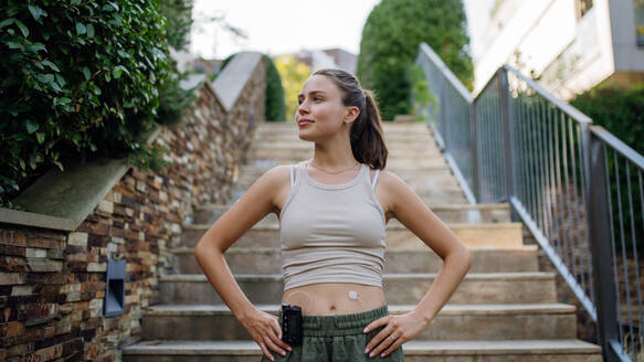 Beautiful diabetic woman preparing for outdoor run in the city. Young woman wearing an insulin pump during exercising. Concept of exercise and diabetes. Banner with copy space. - HPIF31379