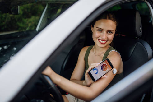 Diabetikerin, die ihren Blutzuckerspiegel vor dem Autofahren überprüft. Diabetikerin, die ihr CGM mit einem Smartphone verbindet, um ihren Blutzuckerspiegel in Echtzeit zu überwachen. - HPIF31384