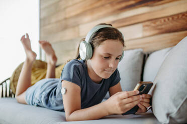 Diabetic girl watching social media content on smart phone.The CGM device makes the life of the schoolgirl. easier, helping manage her illness and focus on other activities. - HPIF31404