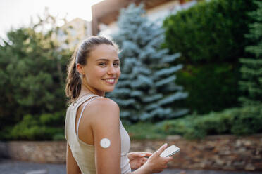 Beautiful diabetic woman preparing for outdoor workout in the city. Young woman with CGM checking her blood sugar level before exercising. Concept of exercise and diabetes. - HPIF31414