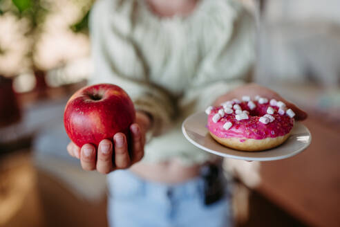 Diabetikerin wählt zwischen einem frischen Apfel und einem süßen Donut. Bedeutung der richtigen Ernährung und Diät bei Diabetes. - HPIF31421