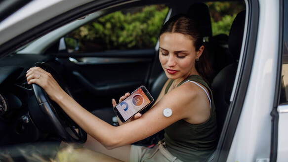 Diabetikerin, die ihren Blutzuckerspiegel vor dem Autofahren überprüft. Diabetikerin, die ihr CGM mit einem Smartphone verbindet, um ihren Blutzuckerspiegel in Echtzeit zu überwachen. - HPIF31422