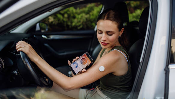 Woman with diabetes checking her blood glucose level before driving a car. Diabetic woman connecting CGM to a smartphone to monitor her blood sugar levels in real time. - HPIF31422