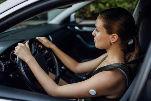 Woman with diabetes monitoring her blood sugar during car drive. Diabetic woman with CGM needs to raise her blood sugar level to continue driving. - HPIF31423