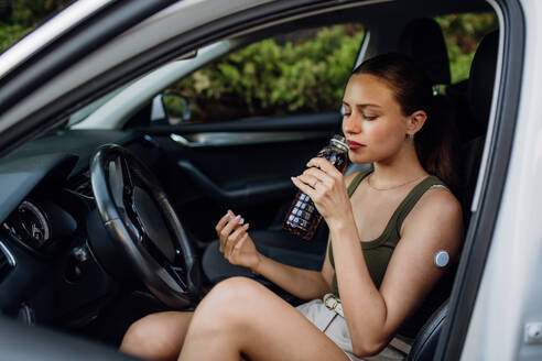 Woman with diabetes feeling dizzy during car drive. Diabetic woman with CGM needs to raise her blood sugar level to continue driving, drinking sweet drink. - HPIF31425