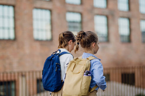 Rückansicht von zwei Schülerinnen auf dem Weg zur Schule, Mitschülerinnen mit Rucksäcken vor dem Schulgebäude. - HPIF31431