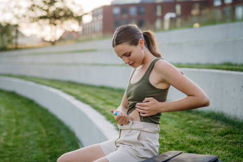 Frau, die sich im Freien im Park Insulin in den Unterleib spritzt. Nahaufnahme einer Frau mit Typ-1-Diabetes, die mit einer Spritze Insulin einnimmt. - HPIF31441