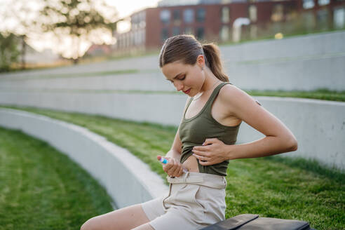 Woman injecting insulin in her abdomen outdoors, in park. Close up of woman with type 1 diabetes taking insuling with syringe needle. - HPIF31441