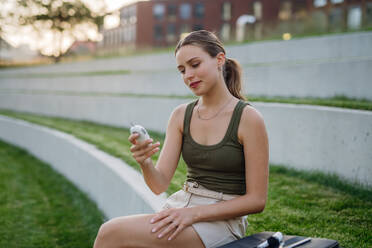 Diabetic woman checking her blood glucose level using a fingerstick glucose meter in public park. Waiting for results from glucometer blood test outdoors in city. - HPIF31442
