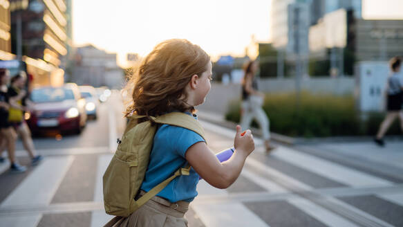 Seitenansicht eines Mädchens mit Rucksack, das auf dem Weg zur Schule den Fußgängerüberweg überquert. Konzept des Schulanfangs. - HPIF31444
