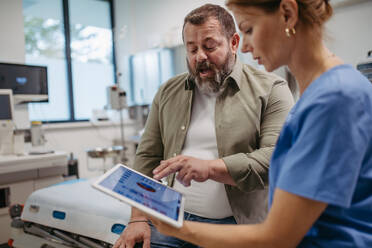 Female doctor consulting with the overweight patient, discussing test result in doctor office. Obesity affecting middle-aged men's health. Concept of health risks of overwight and obesity. - HPIF31465