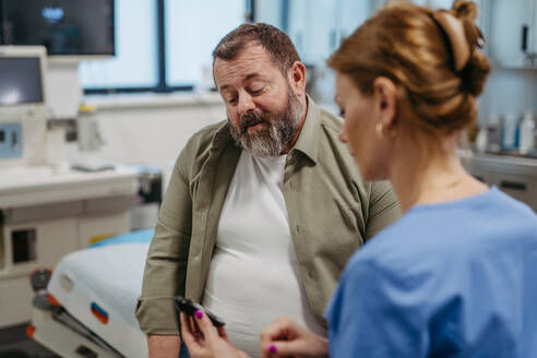 Ein Arzt prüft den Blutzuckerspiegel mit einem Glukosemessgerät, während er auf die Ergebnisse des Glukosemessgeräts wartet. Ein übergewichtiger Mann mit dem Risiko, an Typ-2-Diabetes zu erkranken. Konzept der Gesundheitsrisiken von Übergewicht und Adipositas. - HPIF31471
