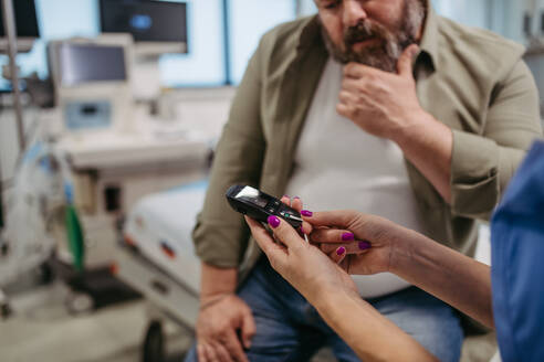 Ein Arzt prüft den Blutzuckerspiegel mit einem Glukosemessgerät, während er auf die Ergebnisse des Glukosemessgeräts wartet. Ein übergewichtiger Mann mit dem Risiko, an Typ-2-Diabetes zu erkranken. Konzept der Gesundheitsrisiken von Übergewicht und Adipositas. - HPIF31472