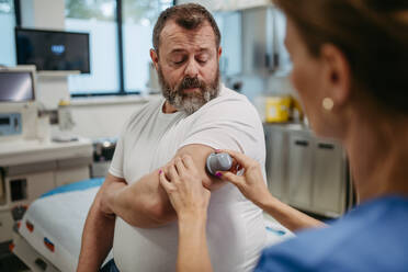 Ein Arzt bringt einen Sensor zur kontinuierlichen Überwachung des Blutzuckerspiegels am Arm eines Patienten an. Ein übergewichtiger oder fettleibiger Mann hat ein erhöhtes Risiko, an Typ-2-Diabetes zu erkranken. Konzept der Gesundheitsrisiken von Übergewicht und Fettleibigkeit. - HPIF31475